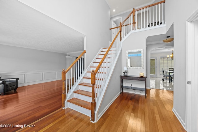 staircase with arched walkways, a notable chandelier, a high ceiling, ornamental molding, and wood-type flooring