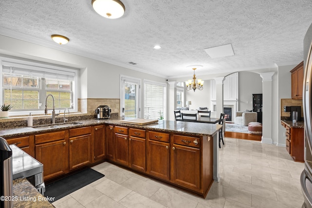 kitchen with a peninsula, dark stone countertops, a sink, and a healthy amount of sunlight