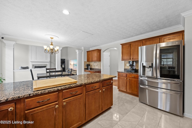 kitchen featuring arched walkways, ornamental molding, dark stone counters, and stainless steel refrigerator with ice dispenser