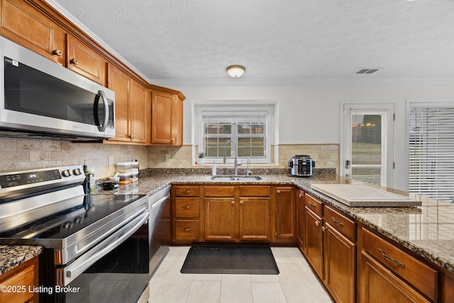 kitchen featuring a healthy amount of sunlight, appliances with stainless steel finishes, dark stone counters, and a sink