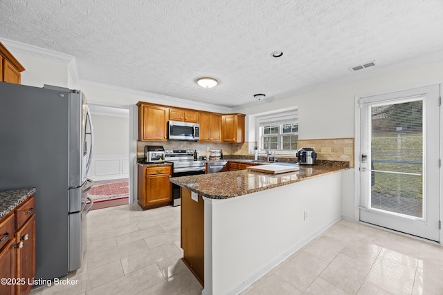 kitchen featuring visible vents, decorative backsplash, appliances with stainless steel finishes, brown cabinetry, and a peninsula