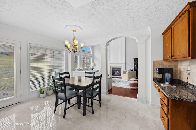 dining room featuring arched walkways, crown molding, decorative columns, an inviting chandelier, and a glass covered fireplace