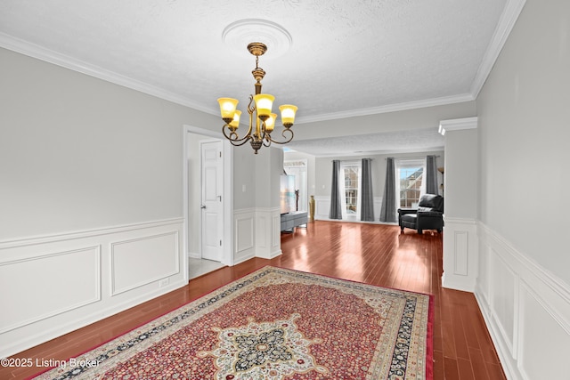 dining space featuring wood finished floors, a textured ceiling, crown molding, a decorative wall, and a notable chandelier