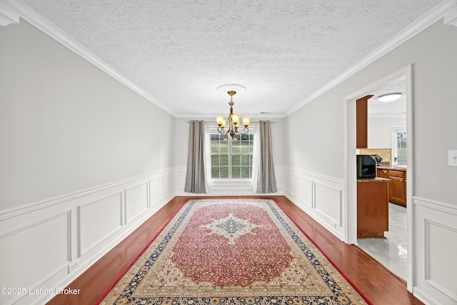 dining area featuring an inviting chandelier, crown molding, a textured ceiling, and wood finished floors