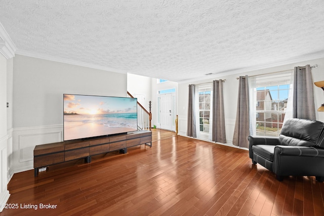 living room with a textured ceiling, a decorative wall, a wainscoted wall, wood finished floors, and crown molding