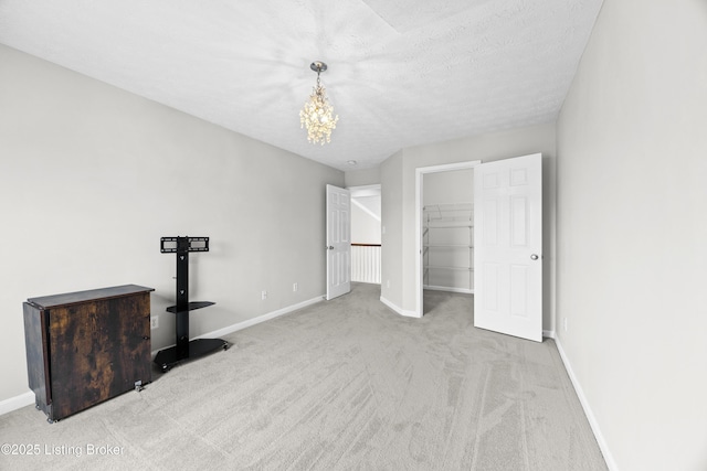 unfurnished bedroom featuring a textured ceiling, a spacious closet, baseboards, and carpet flooring