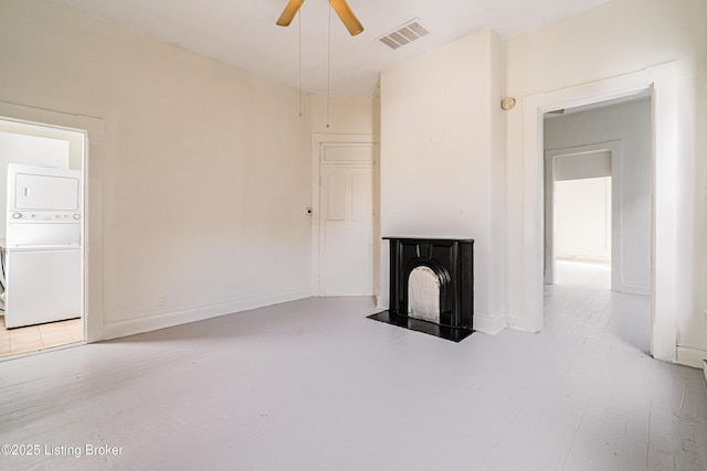 unfurnished living room featuring a fireplace with flush hearth, visible vents, baseboards, a ceiling fan, and stacked washing maching and dryer
