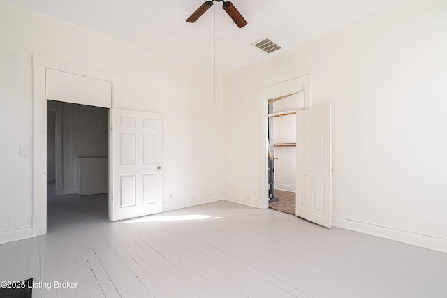 empty room with ceiling fan, wood finished floors, visible vents, and baseboards