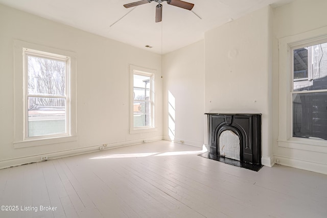 unfurnished living room with a fireplace, plenty of natural light, wood-type flooring, and a ceiling fan