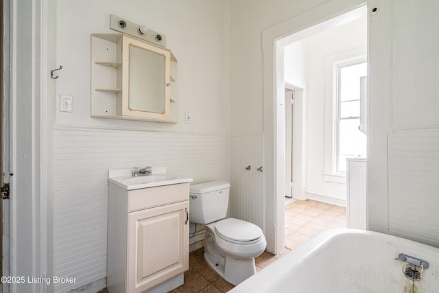 full bathroom with toilet, a bathing tub, vanity, and wainscoting