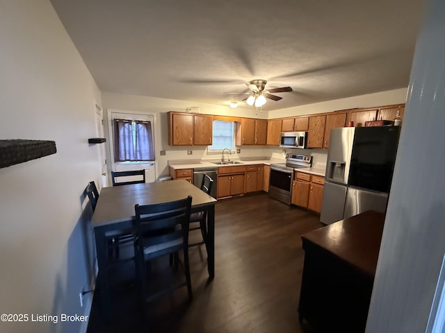 kitchen with a ceiling fan, a sink, light countertops, dark wood-type flooring, and appliances with stainless steel finishes