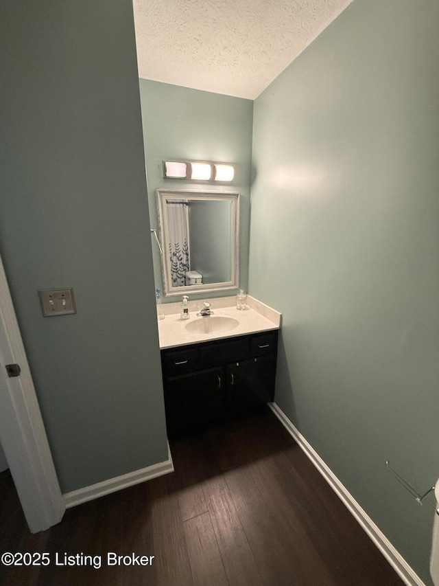 bathroom featuring baseboards, a textured ceiling, wood finished floors, and vanity