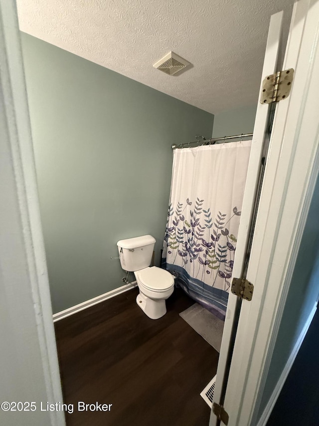 bathroom with visible vents, toilet, a shower with shower curtain, wood finished floors, and a textured ceiling