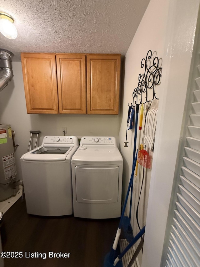 laundry area featuring washing machine and clothes dryer, cabinet space, water heater, dark wood-type flooring, and a textured ceiling