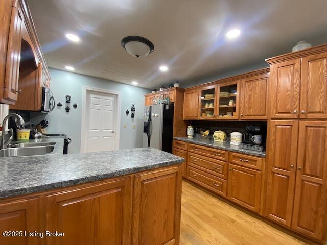 kitchen with brown cabinets, stainless steel appliances, dark countertops, a sink, and light wood-type flooring