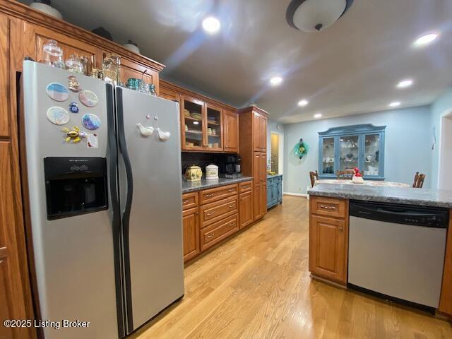 kitchen featuring light wood finished floors, glass insert cabinets, brown cabinets, stainless steel appliances, and recessed lighting