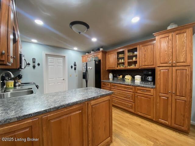 kitchen with dark countertops, brown cabinets, fridge with ice dispenser, light wood-style floors, and a sink