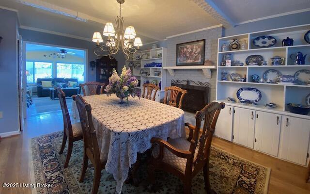 dining space with a fireplace, wood finished floors, built in features, ornamental molding, and an inviting chandelier