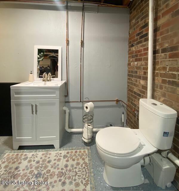 bathroom featuring brick wall, vanity, and toilet