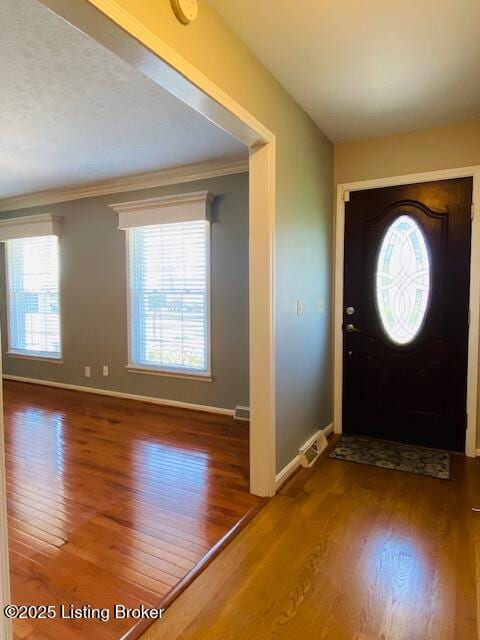 foyer featuring wood finished floors, visible vents, crown molding, and baseboards
