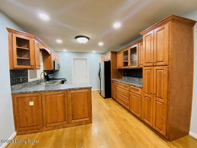kitchen featuring a sink, brown cabinets, glass insert cabinets, a peninsula, and freestanding refrigerator