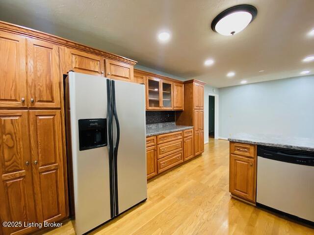 kitchen with light wood finished floors, glass insert cabinets, dishwashing machine, brown cabinets, and stainless steel fridge with ice dispenser