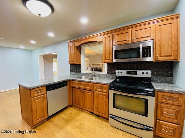 kitchen with brown cabinetry, backsplash, appliances with stainless steel finishes, and a sink