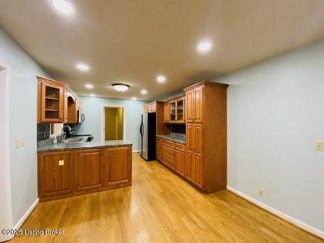 kitchen featuring light wood finished floors, a peninsula, freestanding refrigerator, glass insert cabinets, and brown cabinets