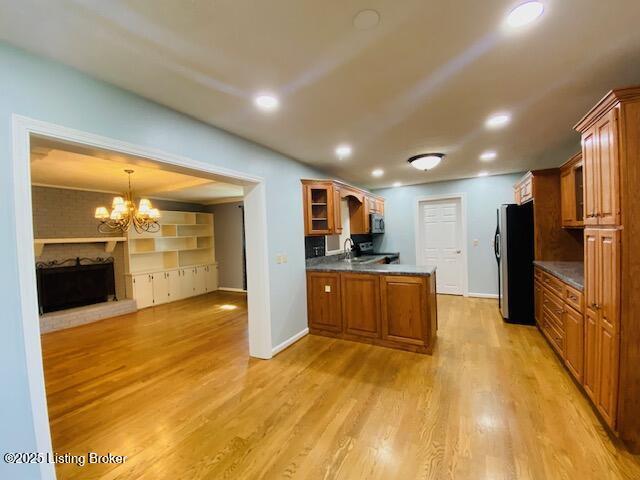 kitchen with brown cabinetry, a peninsula, freestanding refrigerator, and glass insert cabinets