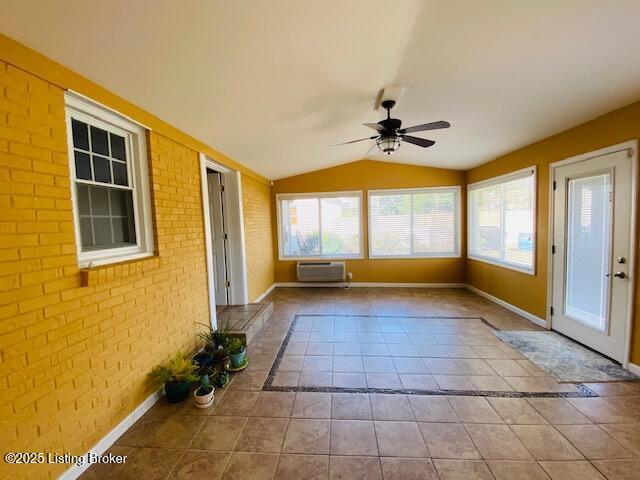 unfurnished sunroom featuring a wall mounted air conditioner, vaulted ceiling, tile patterned flooring, and brick wall