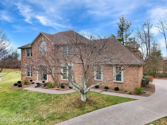 view of front of house with a front yard, brick siding, and roof with shingles