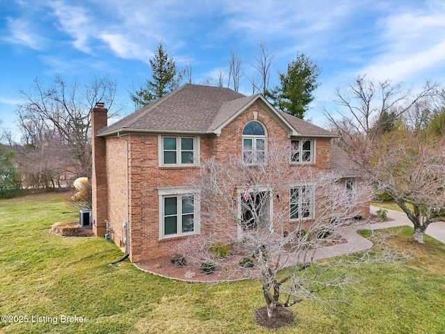 view of front facade with central AC unit, brick siding, a shingled roof, a chimney, and a front yard