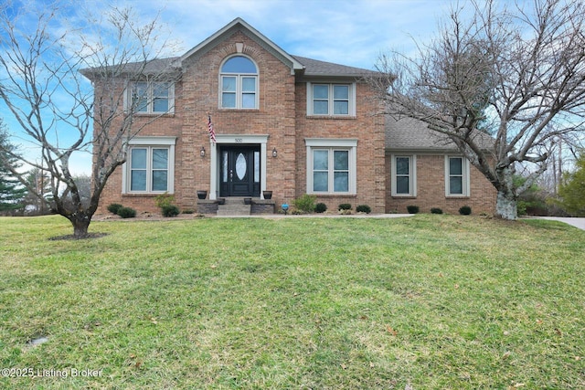 colonial house featuring brick siding, a front yard, and a shingled roof