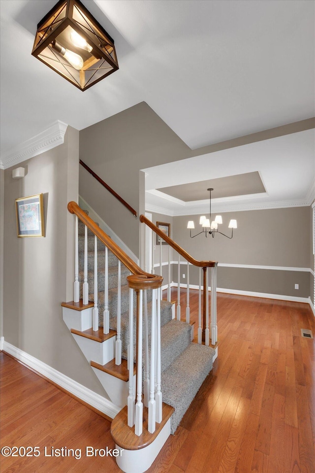 staircase with a raised ceiling, baseboards, visible vents, and hardwood / wood-style floors