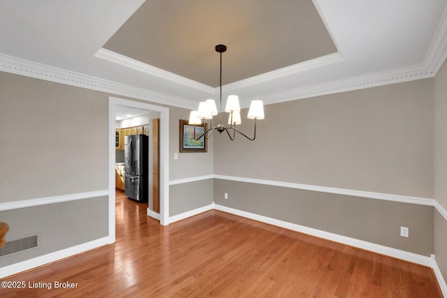 unfurnished dining area with wood finished floors, a raised ceiling, visible vents, and baseboards