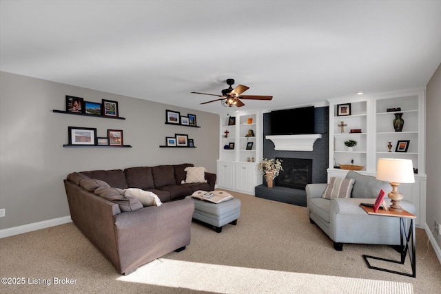 carpeted living room with built in shelves, a fireplace, a ceiling fan, and baseboards