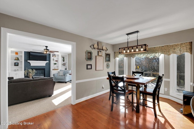 dining area with built in features, a fireplace, a ceiling fan, baseboards, and hardwood / wood-style flooring