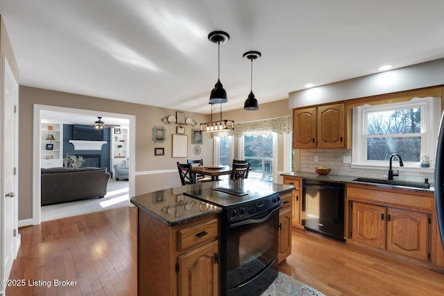 kitchen with a sink, light wood-style floors, black appliances, tasteful backsplash, and a glass covered fireplace