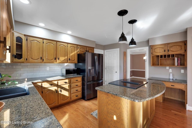 kitchen featuring stone counters, a kitchen island, appliances with stainless steel finishes, decorative backsplash, and light wood finished floors