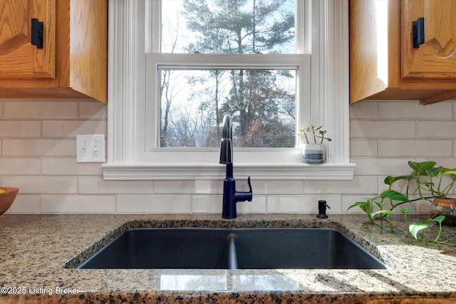 kitchen with light stone counters, brown cabinets, a sink, and backsplash