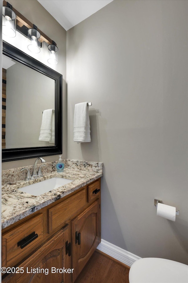 half bathroom with wood finished floors, vanity, toilet, and baseboards