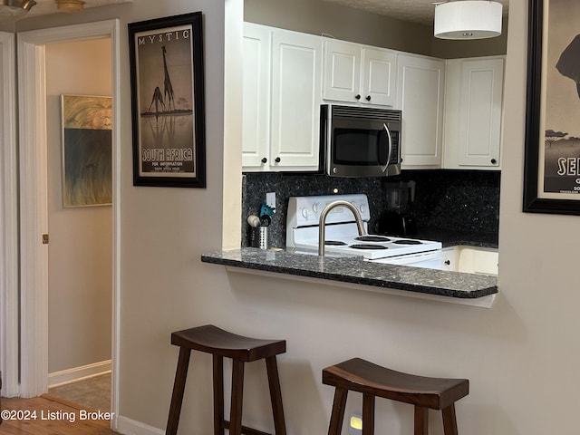 kitchen with a breakfast bar area, white electric range, white cabinets, decorative backsplash, and stainless steel microwave