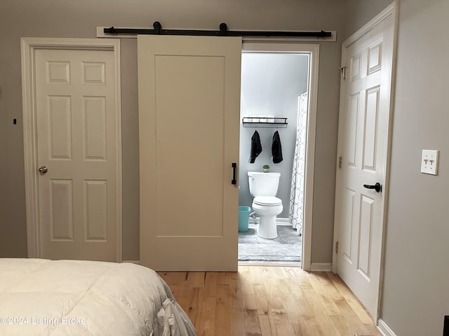 bedroom featuring light wood-type flooring, a barn door, and ensuite bathroom