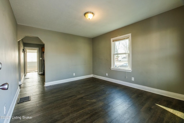 spare room featuring baseboards, visible vents, dark wood finished floors, and arched walkways