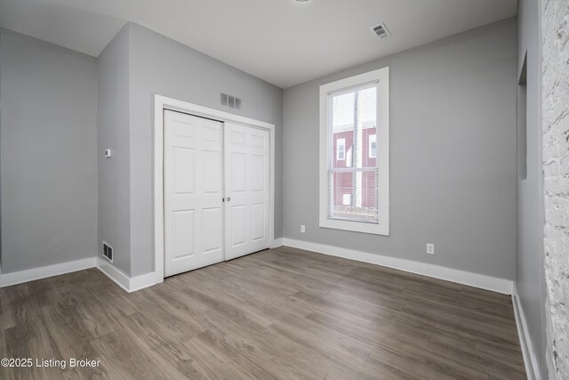 unfurnished bedroom with a closet, visible vents, baseboards, and wood finished floors