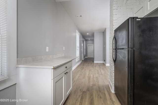 kitchen with baseboards, light wood-style floors, light countertops, white cabinets, and freestanding refrigerator