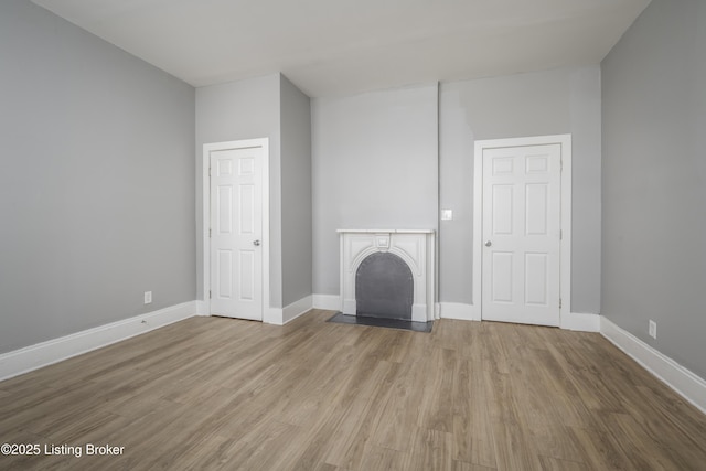 unfurnished living room featuring a fireplace, baseboards, and wood finished floors