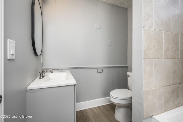 bathroom with toilet, a wainscoted wall, wood finished floors, a textured ceiling, and vanity