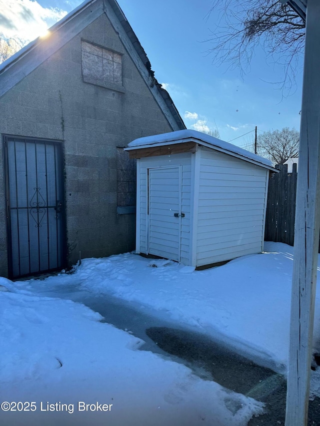 snow covered structure with a storage unit, an outdoor structure, and fence