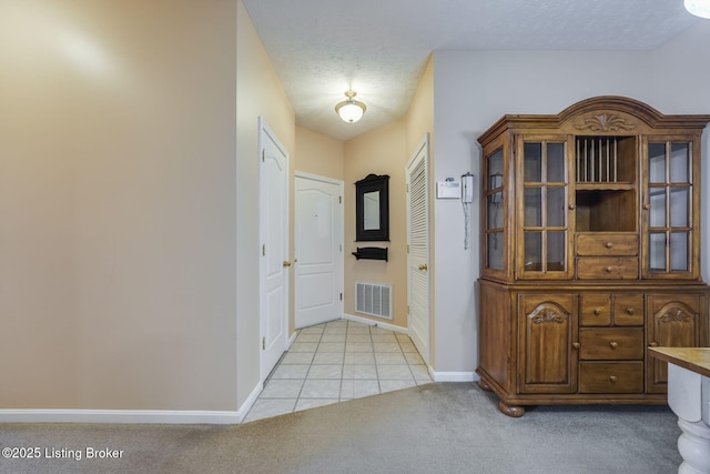 hall with visible vents, baseboards, tile patterned floors, carpet, and a textured ceiling